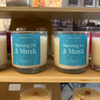 Candles with labels on a wooden shelf, with 'Quien Soy Shoppe' branding in the background.