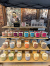 Shelves displaying various candles with colorful labels against a graffiti-covered wall.