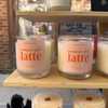 Candles labeled 'pumpkin spice latte' on a shelf with a blurred background