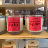 Candles with 'Spiced Cran-Apple Spritz' labels on a wooden shelf.